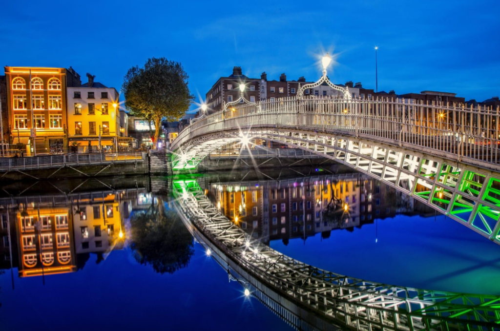 The historic Ha'penny Bridge illuminated at blue hour with colorful reflections in the River Liffey in Dublin, Ireland.
