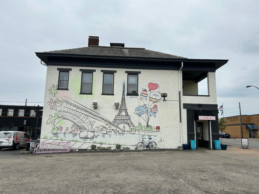 Paris-themed mural with the Eiffel Tower, pastel cupcakes, a bridge, and a river at Très Belle Cakes in Reading, Ohio.
