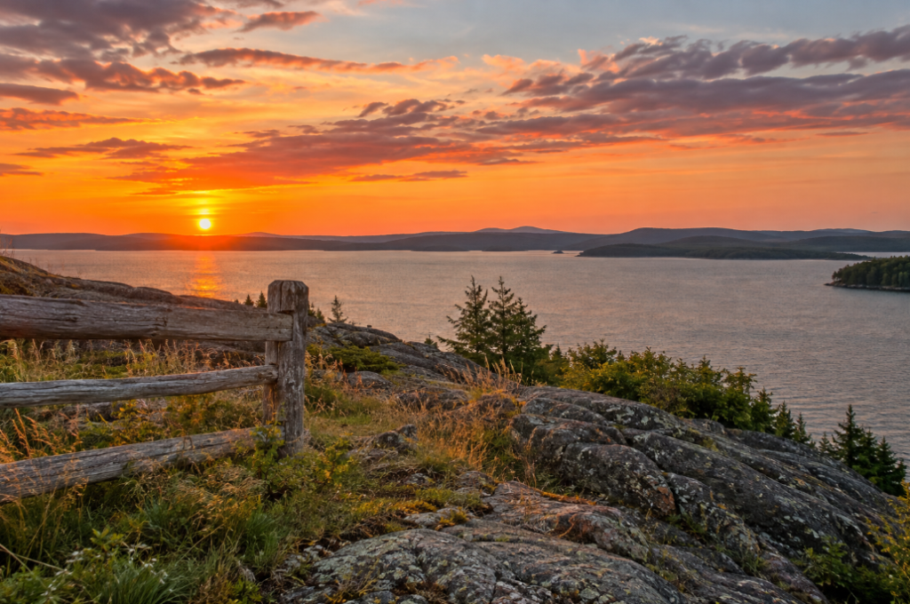 Colorful sunset over a lake with illuminated rocks, grasses and a wooden fence in the foreground