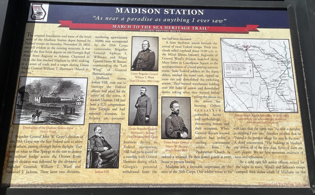 Interpretive sign at Madison Station in Madison, Georgia, detailing the site’s role in the Civil War as part of Sherman’s “March to the Sea.” The sign includes historic images, portraits of Union generals, a map of Union troop movements, and a quote calling Madison “as near a paradise as anything I ever saw.” It describes the burning of the depot by Federal troops on November 19, 1864, and notes the efforts of Mayor Joshua Hill to spare the town from greater destruction. Part of the Georgia Civil War Heritage Trails series.
Interpretive sign at Madison Station in Madison, Georgia, detailing the site’s role in the Civil War as part of Sherman’s “March to the Sea.” The sign includes historic images, portraits of Union generals, a map of Union troop movements, and a quote calling Madison “as near a paradise as anything I ever saw.” It describes the burning of the depot by Federal troops on November 19, 1864, and notes the efforts of Mayor Joshua Hill to spare the town from greater destruction. Part of the Georgia Civil War Heritage Trails series.