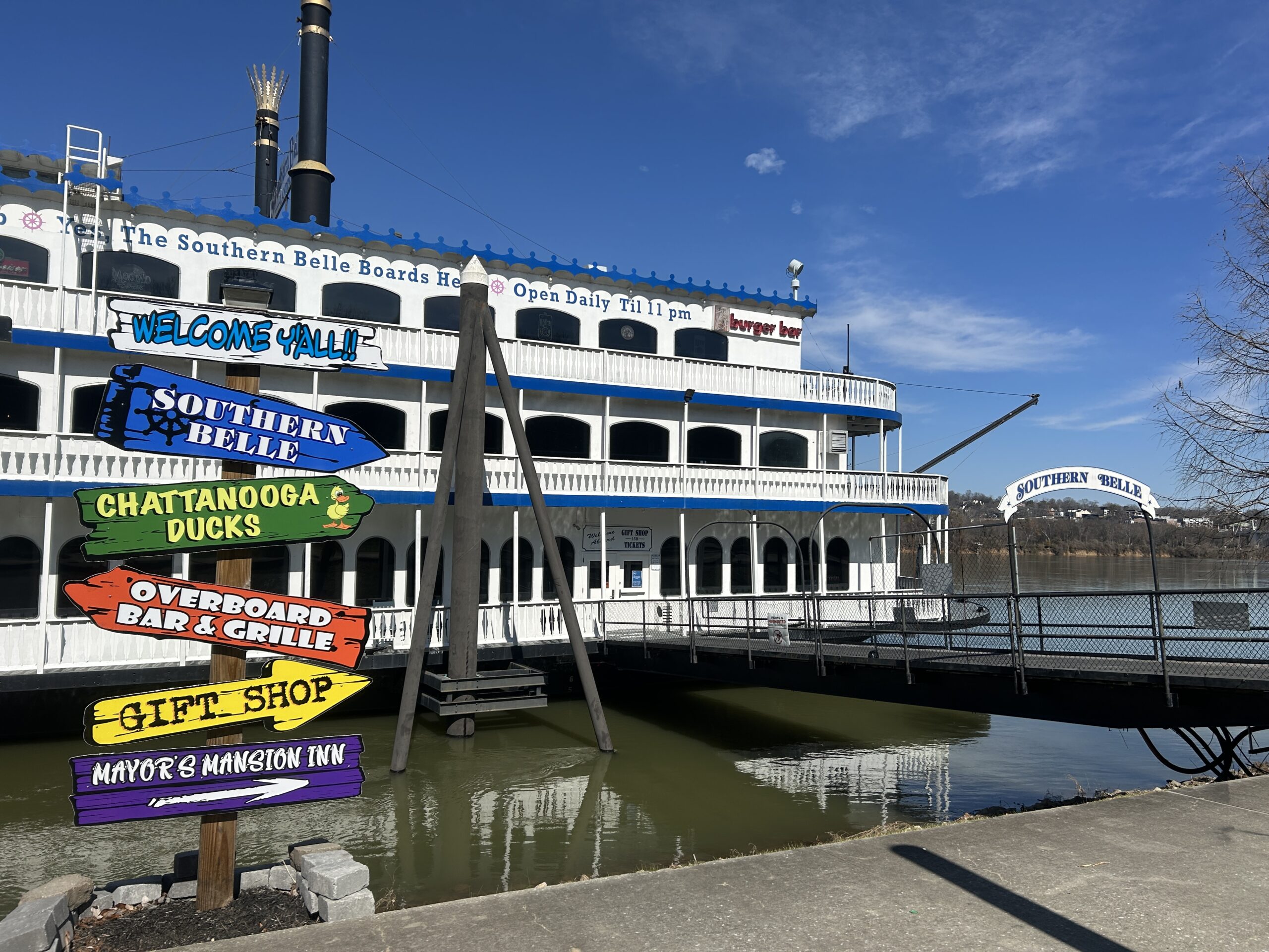 Photo of the Southern Belle Riverboat docked in Chattanooga, Tennessee, with colorful directional signs in the foreground and a clear blue sky overhead.