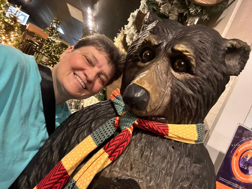 Visitor taking a selfie with a bear statue wearing a winter scarf at The Incredible Christmas Place