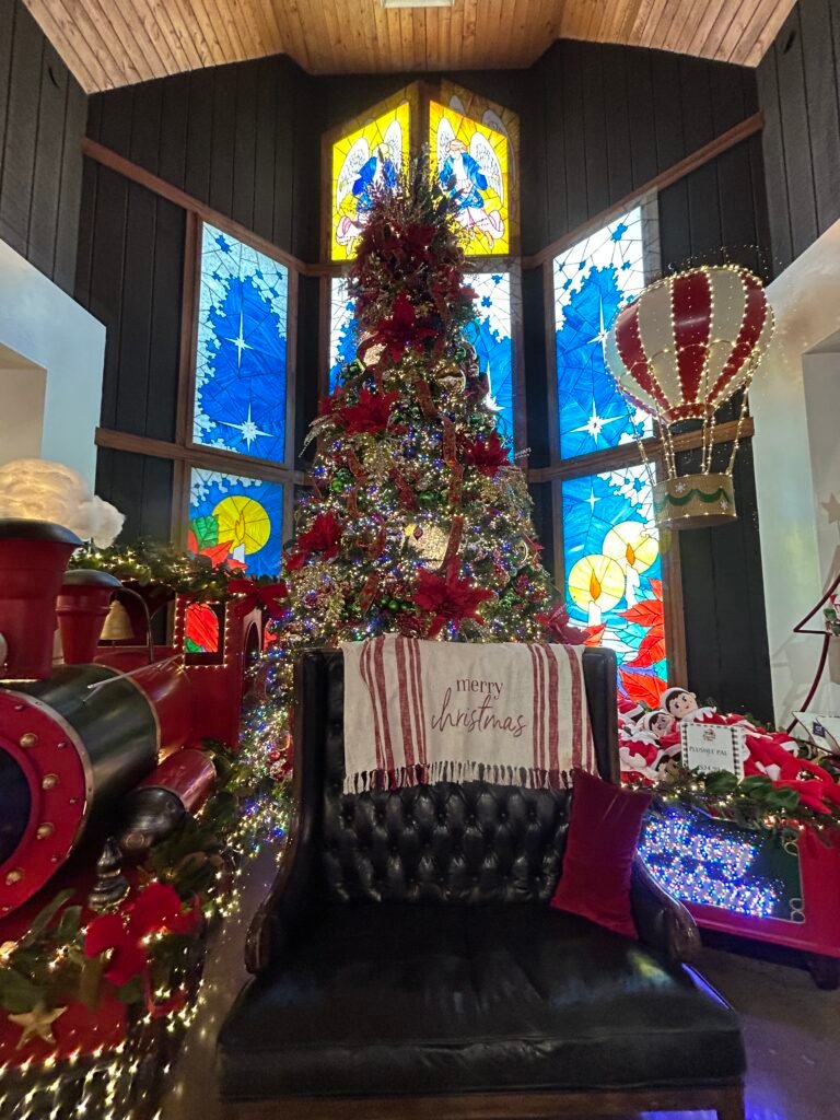 Christmas tree display with a large train engine set against stained-glass windows at The Incredible Christmas Place