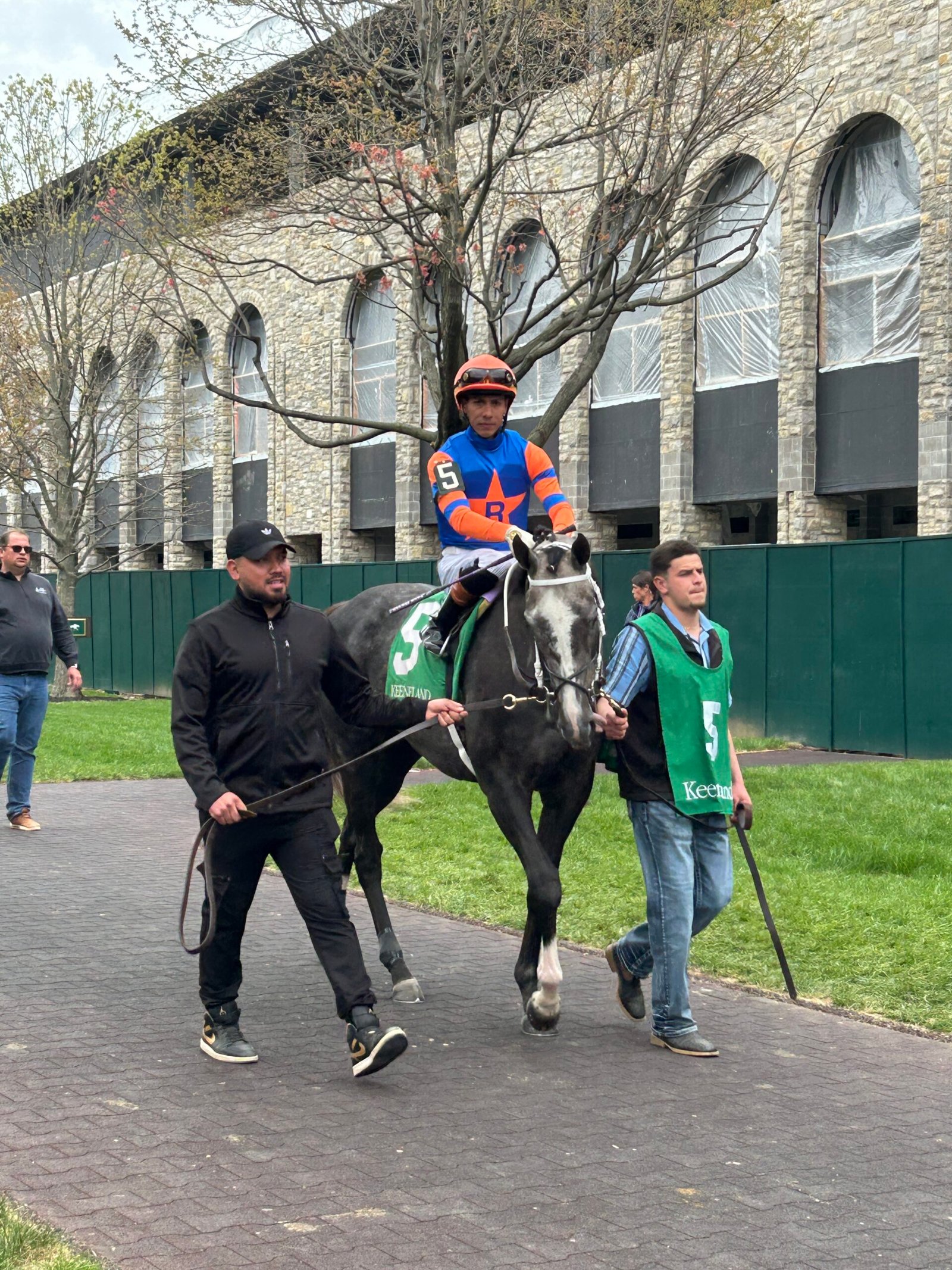 Jockey seated on a racehorse being led by two handlers near the paddock at Keeneland in Lexington, Kentucky.