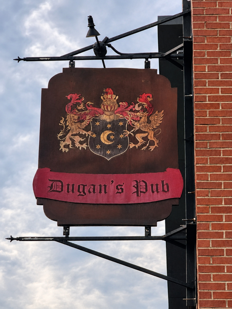Decorative hanging sign for Dugan's Pub featuring a heraldic coat of arms mounted on a brick building in Wichita, Kansas.