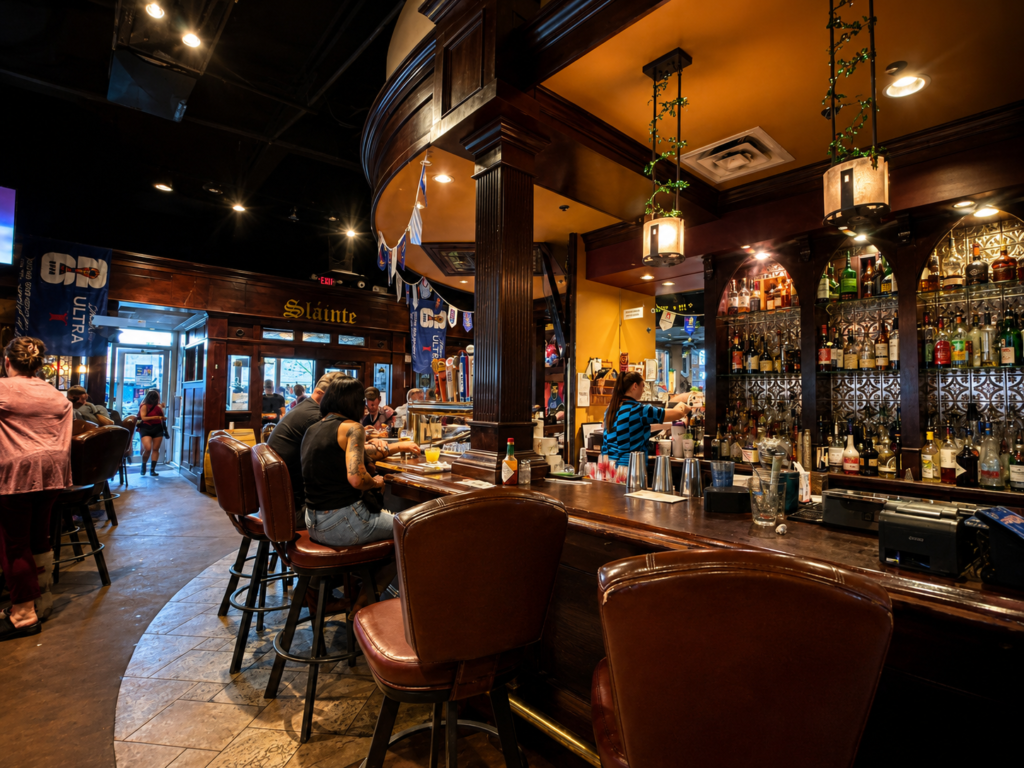 Curved wooden bar inside Dugan's Pub in Wichita, Kansas, featuring leather bar stools, handcrafted woodwork, hanging lanterns, and a well-stocked liquor display.
