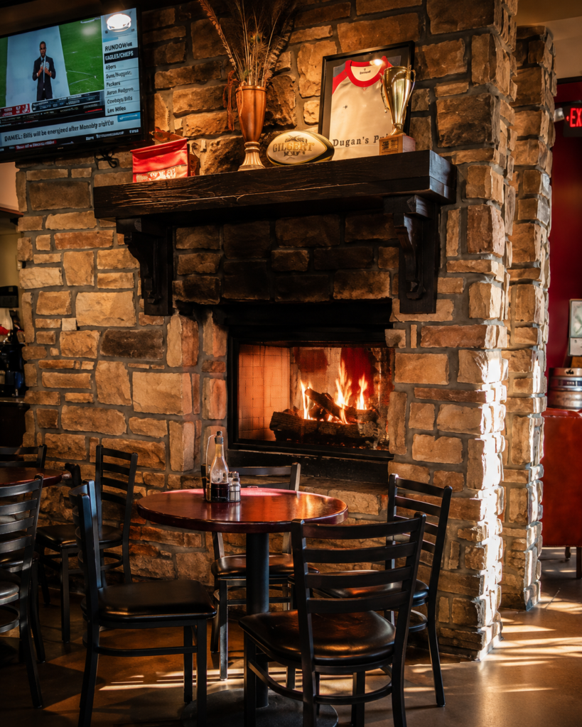 Stone fireplace inside Dugan's Pub in Wichita, Kansas, creating a warm and inviting atmosphere with rustic stonework, a wooden mantel, and cozy seating.