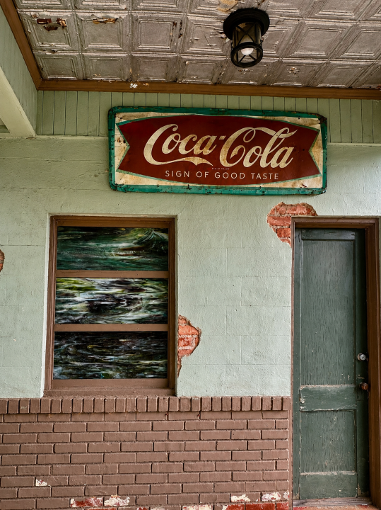 Weathered Coca-Cola “Sign of Good Taste” above a green doorway and exposed brick at an old Watkinsville service station.
