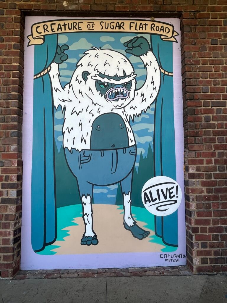 Illustrated Creature of Sugar Flat Road mural showing a white furry character emerging between theatrical curtains.