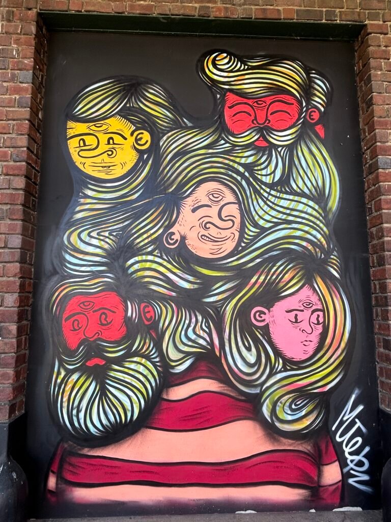 Whimsical mural of a woman whose long, flowing striped hair surrounds five colorful faces.