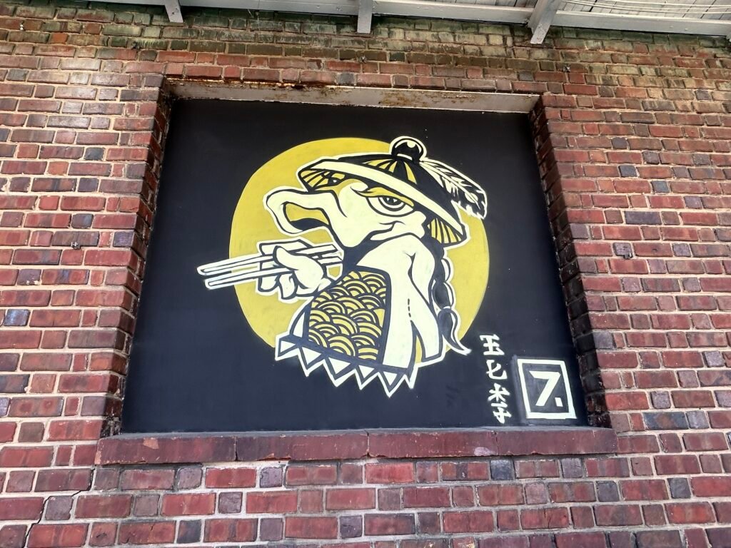 Stylized bird wearing a cap and eating noodles with chopsticks against a black-and-yellow background.