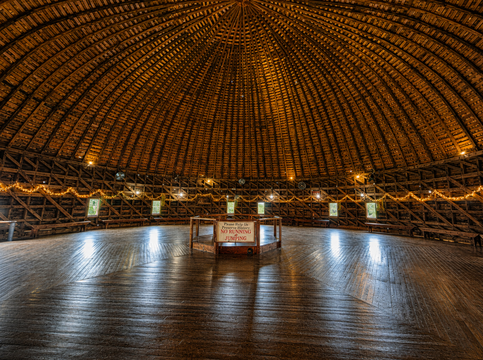 Curved wooden rafters forming the domed ceiling above the polished loft floor inside the Arcadia Round Barn.