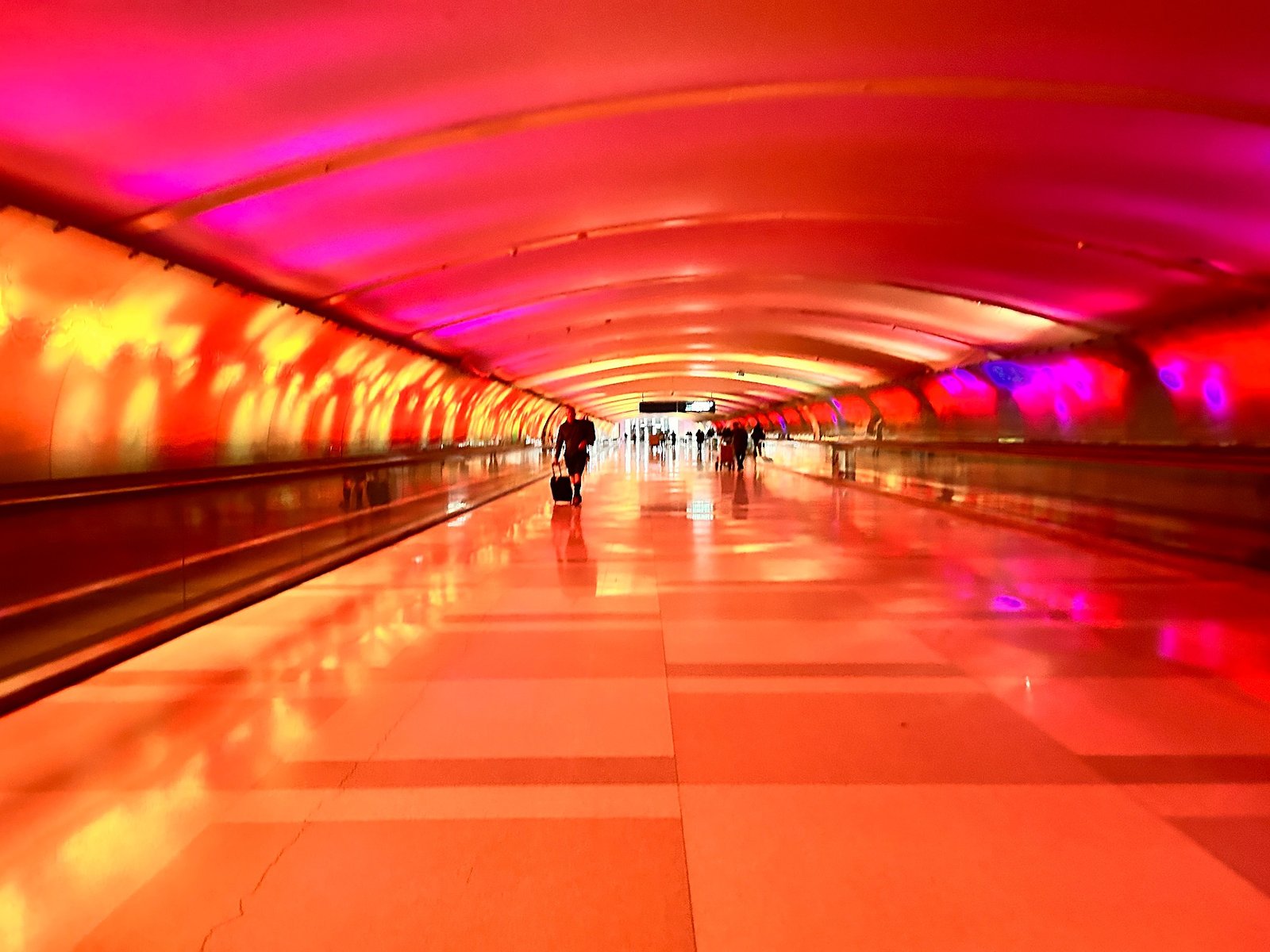 Travelers walk through the red and orange illuminated tunnel in Detroit Airport’s McNamara Terminal.