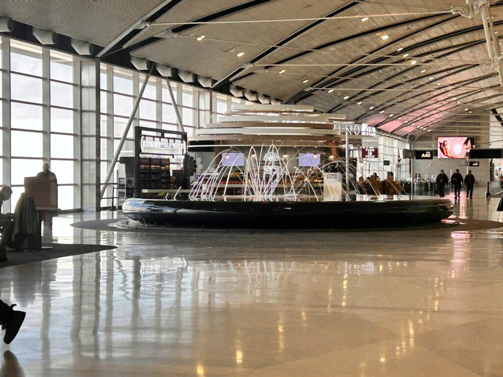 Travelers walk past the arcing water feature inside Detroit Metropolitan Airport’s McNamara Terminal.