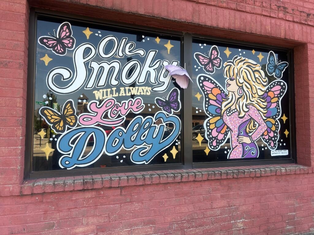 Painted downtown Sevierville window reading Ole Smoky Will Always Love Dolly with Dolly Parton and colorful butterflies