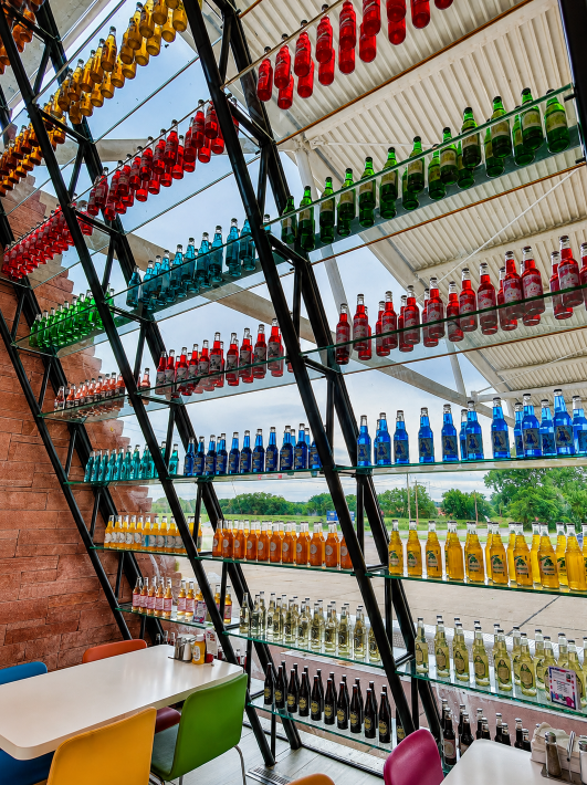 Rows of colorful soda bottles displayed along the glass wall beside dining tables inside POPS 66 in Arcadia, Oklahoma.