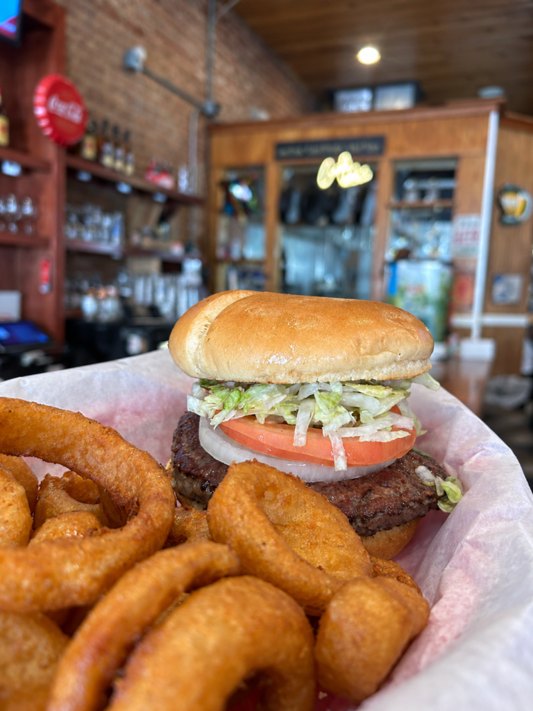 Burger with lettuce, tomato, and onion served with thick-cut onion rings at The Tipsy Turtle