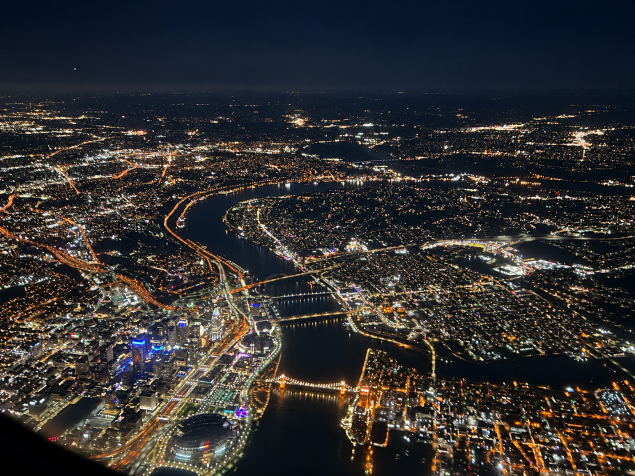 Aerial nighttime view of Cincinnati and the Ohio River with illuminated bridges, photographed through an airplane window after takeoff.