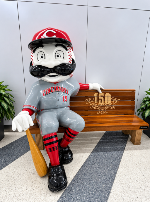 Mr. Redlegs, the Cincinnati Reds mascot, sits on a commemorative wooden bench at CVG Airport.