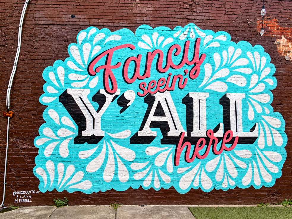 Fancy Seein’ Y’ALL Here mural with turquoise floral patterns, pink script and bold black-and-white lettering on a brick wall in downtown Chattanooga.