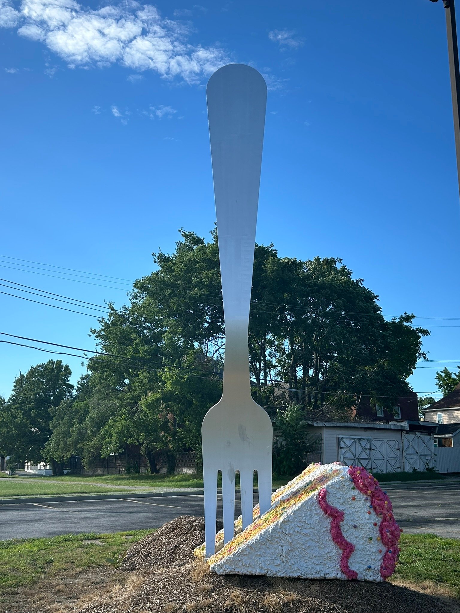Giant silver fork sculpture standing beside an oversized slice of cake at the Fork in the Road attraction in Granite City, Illinois