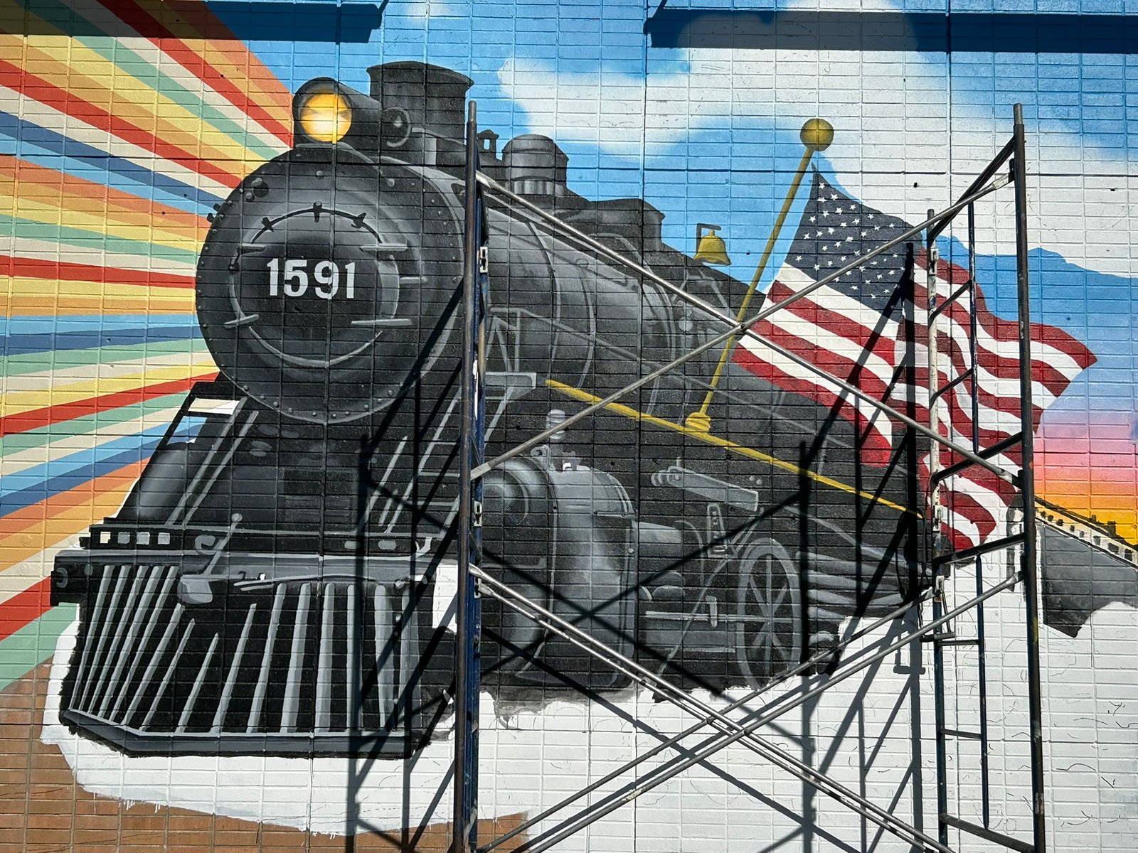 Close-up of The Liberty Express steam locomotive number 1591 and American flag, crossed by restoration scaffolding.