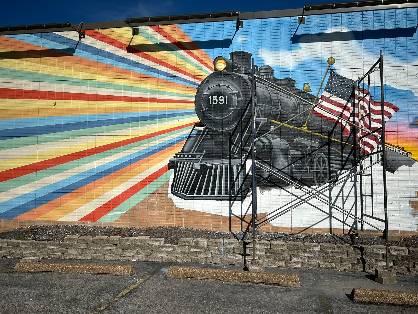 Colorful red, yellow, teal and blue rays spread across The Liberty Express mural toward black steam locomotive 1591.