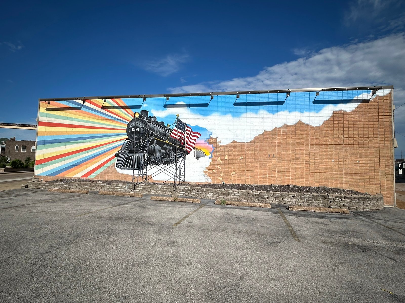 Wide view of The Liberty Express mural in Granite City with steam locomotive 1591, colorful rays, and scaffolding in June 2026.
