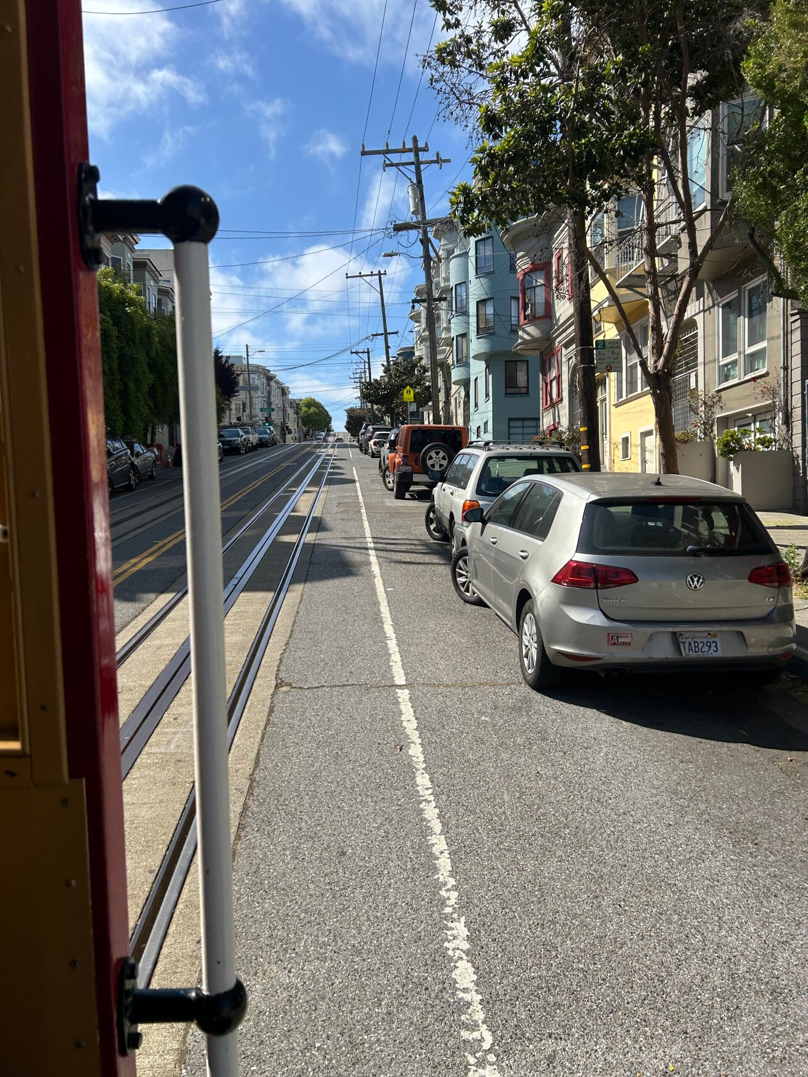 View from the open side of a San Francisco cable car showing tracks, city streets, and the exterior riding area