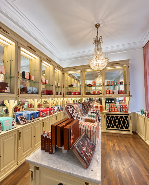Traditional Belgian chocolate shop interior with cream-colored display cabinets, boxed chocolates and a crystal chandelier